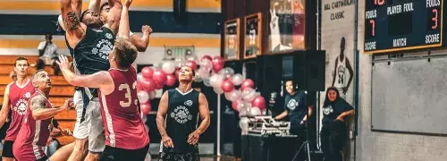 Basketball players jumping up under the hoop going for a ball.